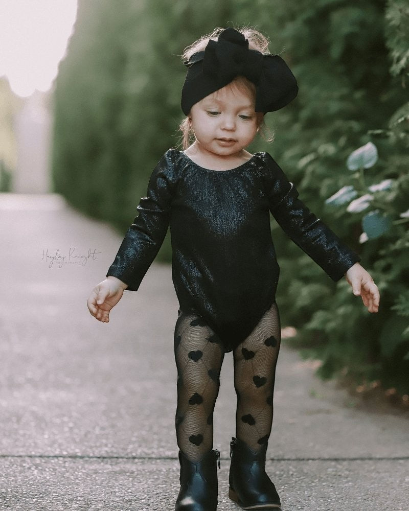 Toddler wearing a Sea Dragon Dreams shimmering black long sleeve leotard with heart-patterned tights and black boots.