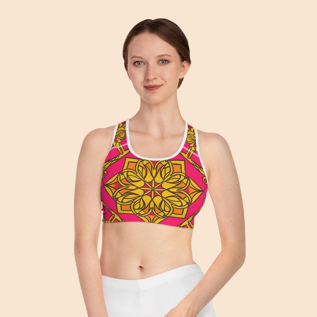 Sea Dragon Dreams Symmetry sports bra with a vibrant pink and gold geometric mandala print and white trim on a model.