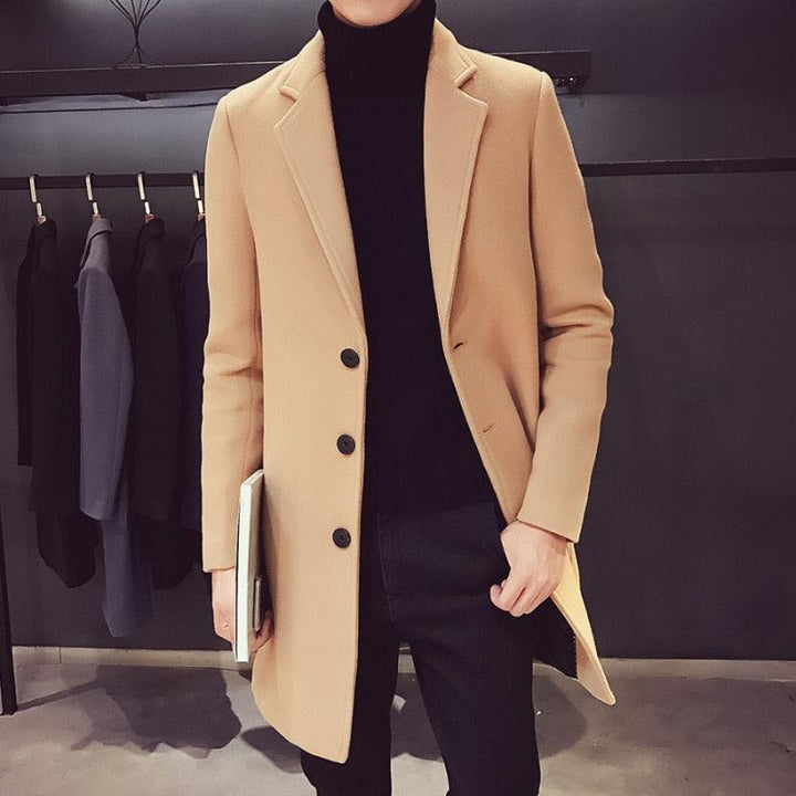 Sea Dragon Dreams men's tan cotton trench coat with a turn-down collar worn over a black turtleneck and trousers.