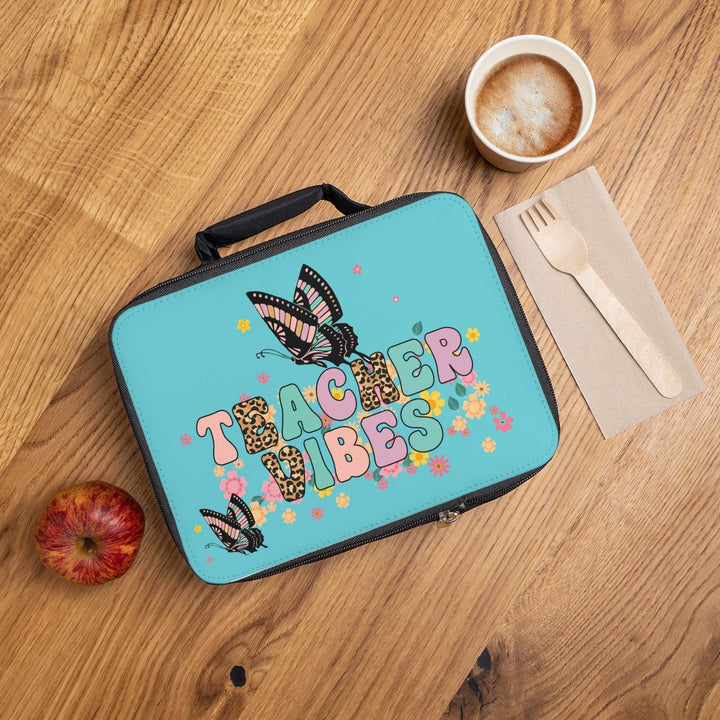 Sea Dragon Dreams Teacher Vibes lunch bag with butterfly and floral print on a wooden desk with an apple and coffee.