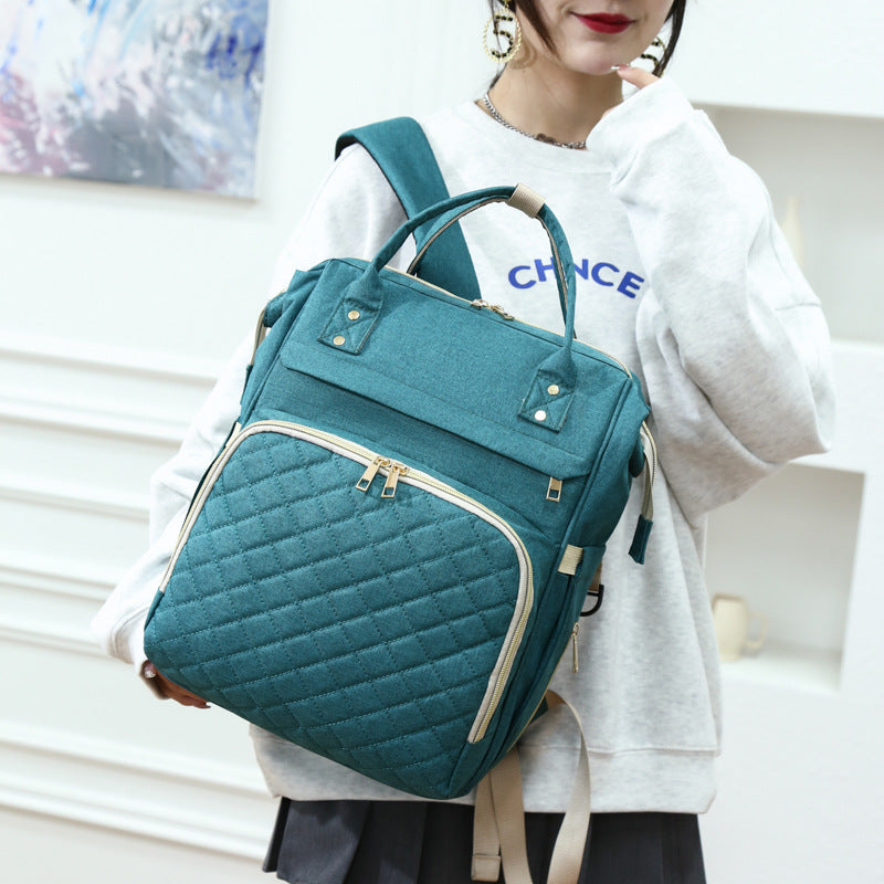 Sea Dragon Dreams teal quilted diaper backpack with gold zippers worn by a woman in a casual white sweatshirt