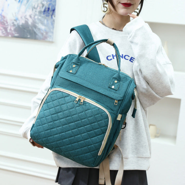 Sea Dragon Dreams teal quilted diaper backpack with gold zippers worn by a woman in a casual white sweatshirt