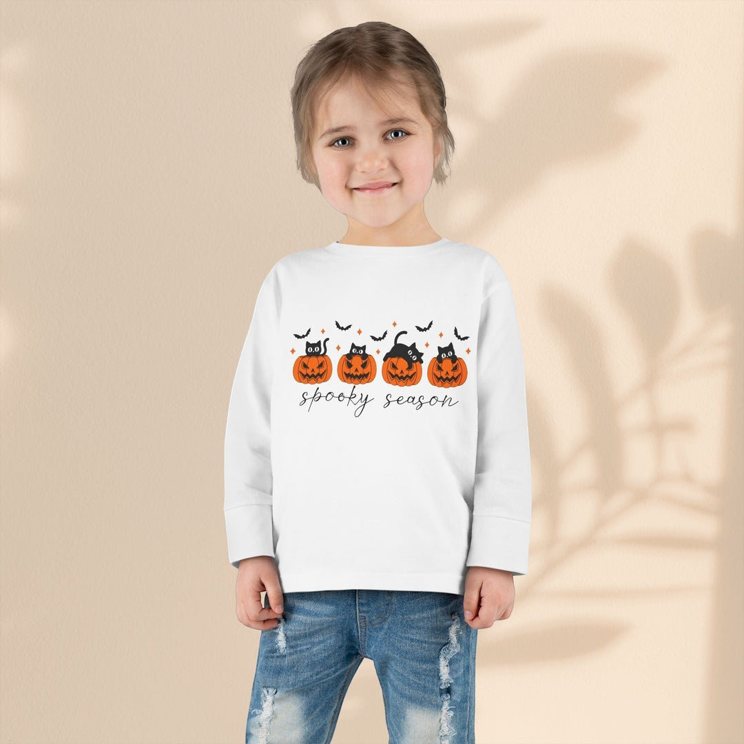 A young girl wearing a Sea Dragon Dreams white long sleeve tee with a spooky season pumpkin and black cat print.
