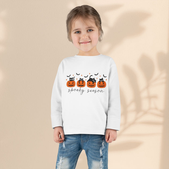 A young girl wearing a Sea Dragon Dreams white long sleeve tee with a spooky season pumpkin and black cat print.