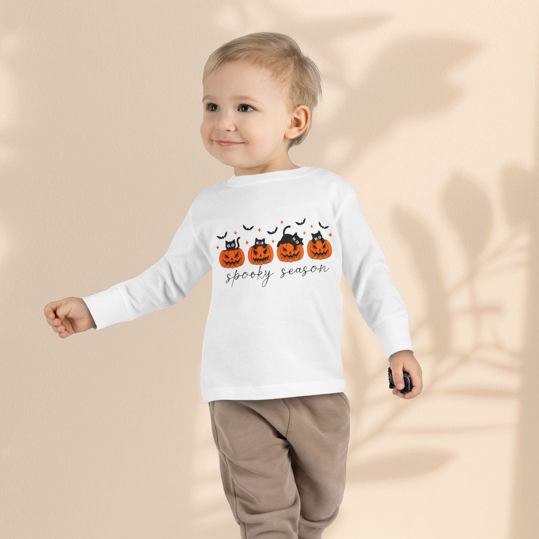 Sea Dragon Dreams toddler wearing a white long sleeve Halloween tee with pumpkin and cat print on a neutral background
