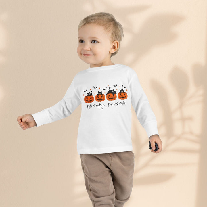 Sea Dragon Dreams toddler wearing a white long sleeve Halloween tee with pumpkin and cat print on a neutral background