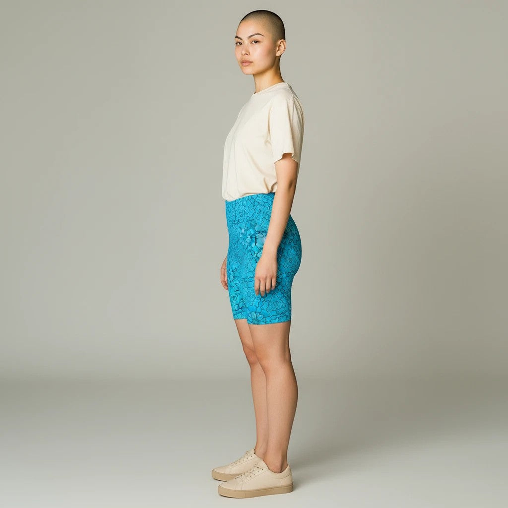 Model wearing Sea Dragon Dreams turquoise groovy print workout shorts with a beige t-shirt and sneakers, side view.