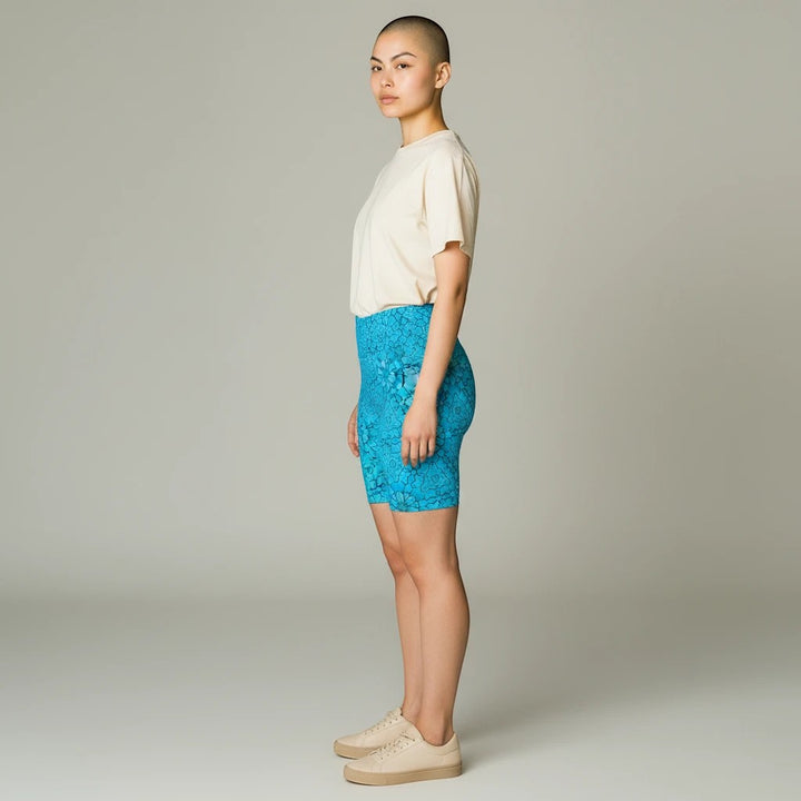 Model wearing Sea Dragon Dreams turquoise groovy print workout shorts with a beige t-shirt and sneakers, side view.