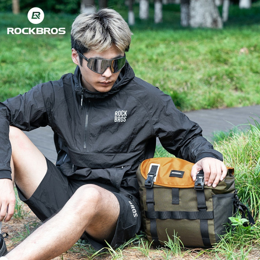 Sea Dragon Dreams 24L waterproof bike bag in olive and tan, featuring durable buckles, resting on grass next to a cyclist.