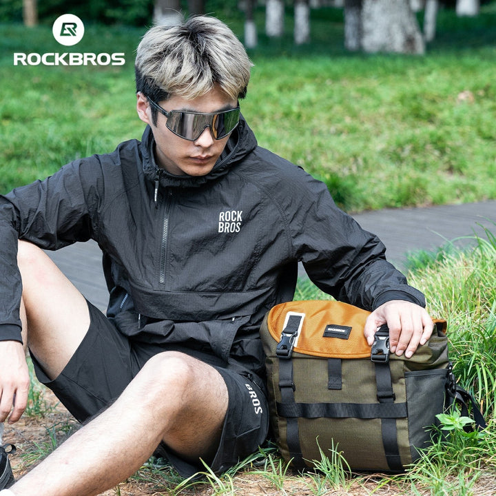 Sea Dragon Dreams 24L waterproof bike bag in olive and tan, featuring durable buckles, resting on grass next to a cyclist.