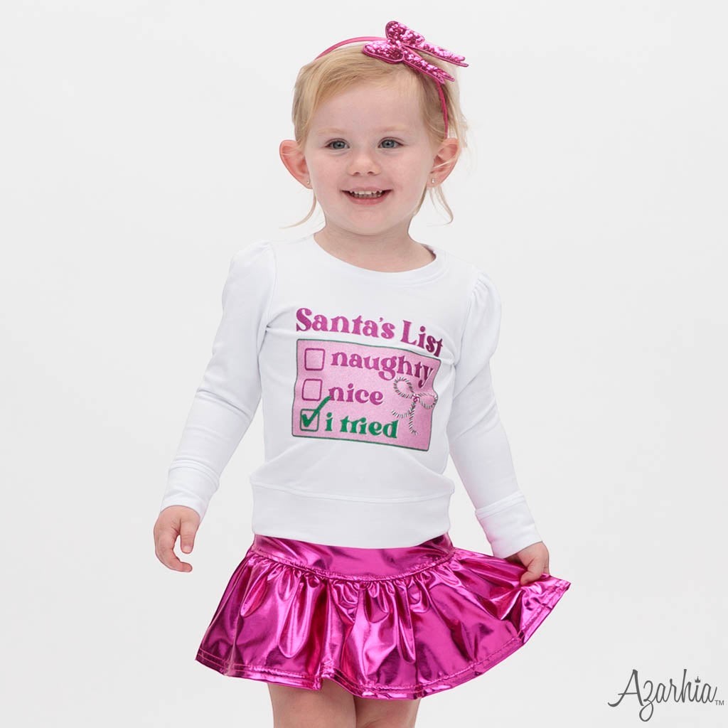 Sea Dragon Dreams white long-sleeve sweatshirt with Santa's List graphic worn by a toddler girl with a pink skirt