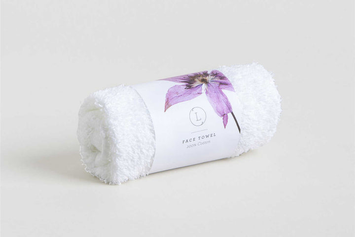 Sea Dragon Dreams white cotton face towel rolled and wrapped in a branded paper band with a purple flower design