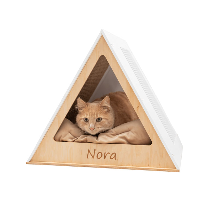 Sea Dragon Dreams modern white wooden triangular cat house with a cozy beige cushion and a cat resting inside.