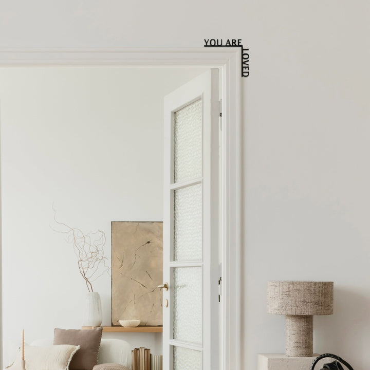 Sea Dragon Dreams wooden corner sign with You Are Loved quote mounted on a white door frame in a minimalist room.