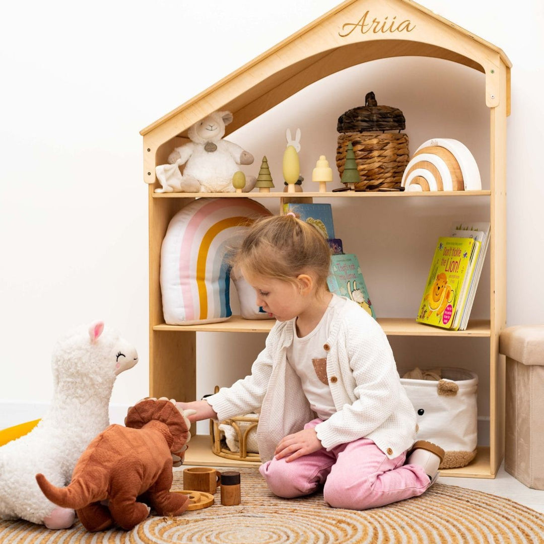 A child playing with toys in front of a Sea Dragon Dreams wooden dollhouse bookcase with personalized name engraving.