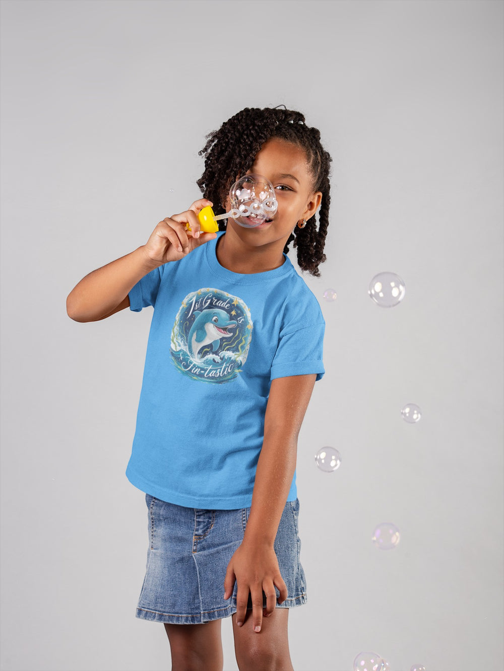 Sea Dragon Dreams youth blue cotton t-shirt with 1st Grade Fintastic dolphin graphic worn by a girl blowing bubbles